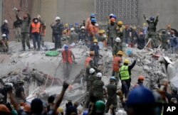 Rescue workers, some holding their arms up as a sign to maintain silence, search for survivors at an apartment building at Amsterdam and Laredo streets that collapsed during an earthquake in the Condesa neighborhood of Mexico City, Mexico, Sept. 21, 2017