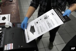 FILE - In this March 17, 2020, file photo a poll worker uses rubber gloves as she enters a ballot in the ballot box at a polling place in Chicago, Illinois. AP Photo/Charles Rex Arbogast, File)