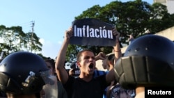 FILE - An opposition supporter holding a placard that reads "Inflation" shouts slogans in front of riot police during a protest in Caracas, Venezuela, March 30, 2017.
