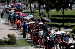 Estadounidenses se resguardan del sol con sombrillas mientras aguardan en fila para presentar sus respetos al fallecido senador John McCain en Phoenix, Arizona, el miércoles, 29 de agosto de 2018.