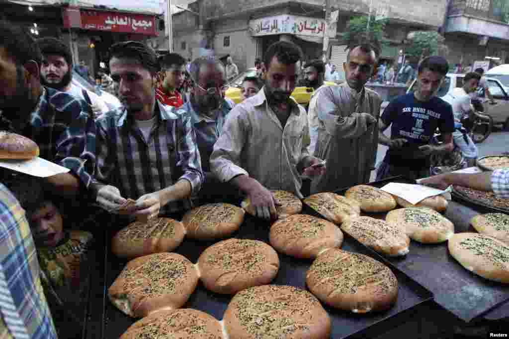 Para pria membeli roti tradisional dari pedagang pinggir jalan di Aleppo, Suriah (10/7). (Reuters/Muzaffar Salman)