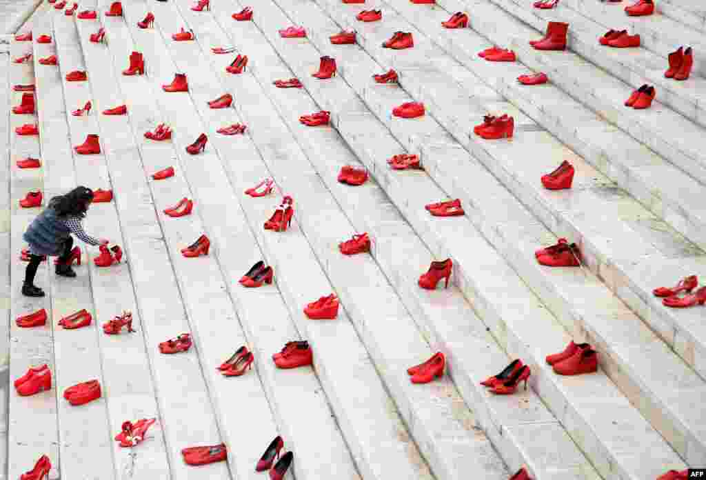 A girl puts flowers at an installation of women&#39;s red shoes displayed on a staircase, as a symbol to denounce violence against women, at Durresi main square in Tirana, Albania, on International Women&#39;s Day.