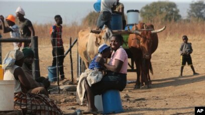 A woman smiles while playing with her baby at a water point on the outskirts of the capital Harare, Nov, 14, 2021.