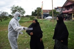 Seorang petugas pemungutan suara (kiri) mengenakan alat pelindung diri membantu para pemilih di Bandung, 9 Desember 2020. (Foto: AFP)