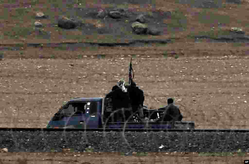 In this image shot with an extreme telephoto lens from the outskirts of Suruc on the Turkey-Syria border, Kurdish fighters with The People&rsquo;s Protection Units, or YPG, the main Kurdish militia in Syria, patrol in a truck along the border road on the outskirts of western Kobani, Syria, during fighting between Syrian Kurds and the militants of Islamic State group, Oct. 17, 2014. 