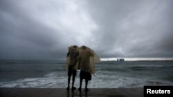 FILE - Two men use a plastic sheet to protect themselves from heavy monsoon rain as they stand by the sea in Colombo, Sri Lanka, May 17, 2018.