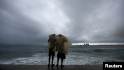 Two men use a plastic sheet to protect themselves from heavy monsoon rain as they stand by the sea in Colombo, Sri Lanka