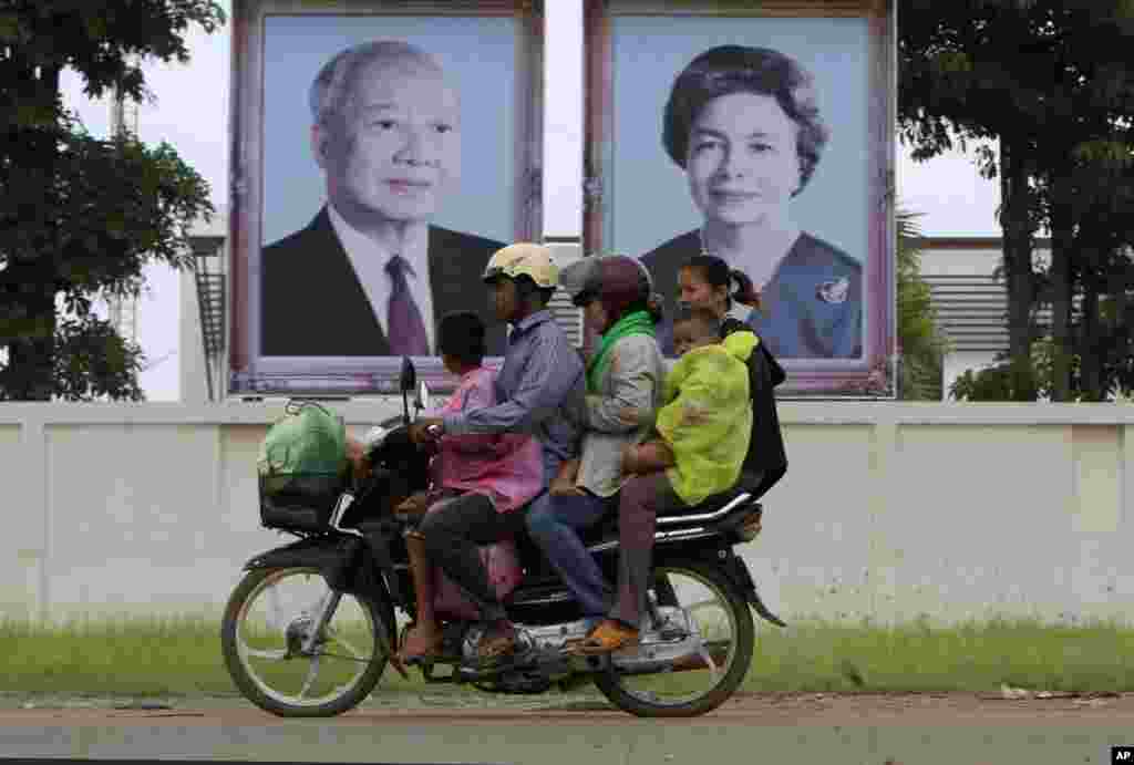 Cambodian family members ride on a motorbike as they head back from their home village, passing by portraits of former King Norodom Sihanouk, left, and his wife Queen Monineath, Phnom Penh, Cambodia, October 15, 2012. 