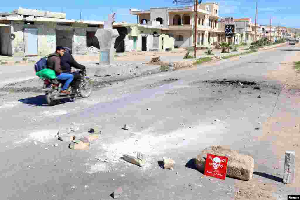 Men ride a motorbike past a hazard sign at a site hit by an airstrike on Tuesday in the town of Khan Sheikhoun, April 5, 2017. The hazard sign reads, &quot;Danger, unexploded ammunition.&quot;