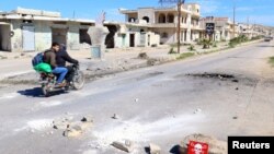 Beberapa pria mengendarai sepeda motor melewati tanda bahaya di lokasi yang dihantam serangan udara baru-baru ini di kota Khan Sheikhoun di provinsi Idlib yang berada di bawah kendali pemberontak, tanggal 5 April 2017 (foto: REUTERS/Ammar Abdullah)