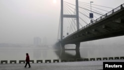 A resident walks along a street on the banks of the Songhua River near a highway bridge on a hazy day in Jilin province, Feb. 25, 2014.