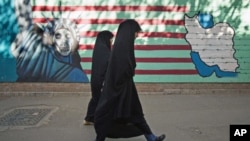 Iranian women walk past an anti-U.S. mural on the wall of the former U.S. embassy in Tehran, Iran, October 12, 2011.