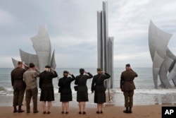 Enthusiasts of England salute in front of The Brave, a monument dedicated to the American soldiers who landed on Omaha Beach on D-Day, in Saint-Laurent-sur-Mer, Tuesday, June 4, 2019, in Normandy.
