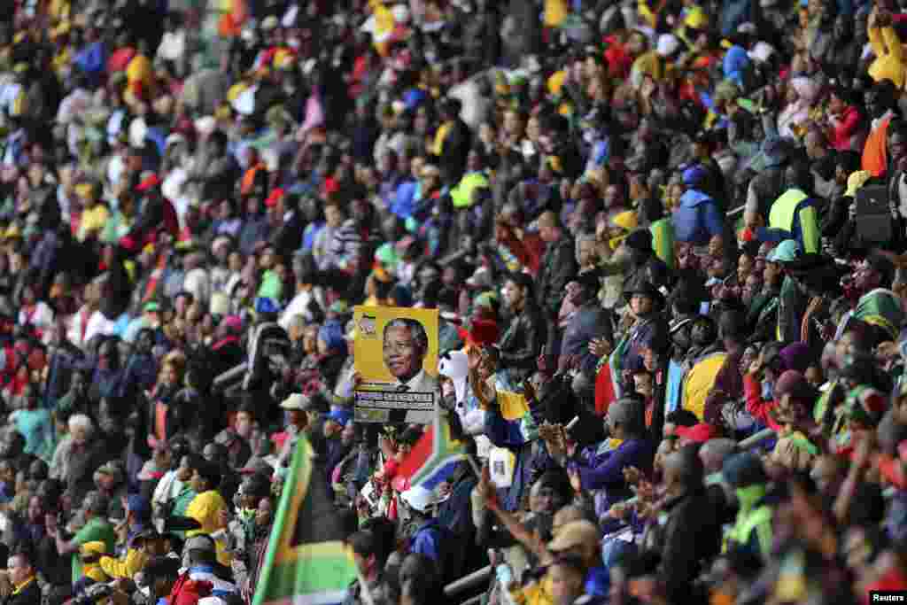 Um homem segura um cartaz com a imagem de Nelson Mandela no Estádio FBN durante a cerimónia fúnebre oficial. Dez. 10, 2013.