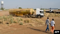 FILE - Two men walk near the Paloch oil fields in Upper Nile State, the site of an oil complex and key crude oil processing facility in the north of the country near the border with Sudan. 