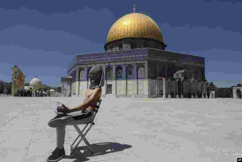A masked Palestinian demonstrator holds a stone during clashes with Israeli security forces in front of the Dome of the Rock Mosque at the Al Aqsa Mosque compound in Jerusalem&#39;s Old City.
