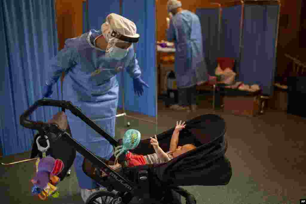A volunteer of the Spanish NGO Open Arms, Julia Martin, plays with four-month old Biel, as his father makes a PCR test for the COVID-19 coronavirus at Vilafranca del Penedes in the Barcelona province, Spain, Aug. 11, 2020.