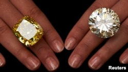 A model poses with a vivid yellow 100.09 carats diamond (L) and a 103.46 carats diamond ring during an auction preview at Sotheby's in Geneva May 7, 2014. These items are expected to reach between CHF 13,250,000 to 22,250,000 (USD 15,000,000 to 25,000,000