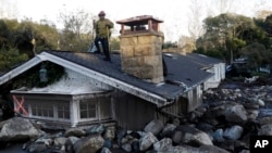 FILE - A firefighter stands on the roof of a house submerged in mud and rocks in Montecito, California, Jan. 10, 2018.