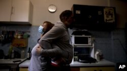 Andrea Cortes demonstrates how she embraces her husband amid the new coronavirus pandemic, while standing in their kitchen in Buenos Aires, Argentina, Monday, July 13, 2020. (AP Photo/Natacha Pisarenko)