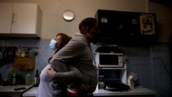 Andrea Cortes demonstrates how she embraces her husband amid the new coronavirus pandemic, while standing in their kitchen in Buenos Aires, Argentina, Monday, July 13, 2020. (AP Photo/Natacha Pisarenko)