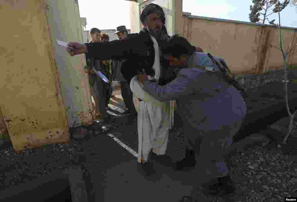 An Afghan policeman searches men before they enter a polling station in Adraskan district, Herat province.