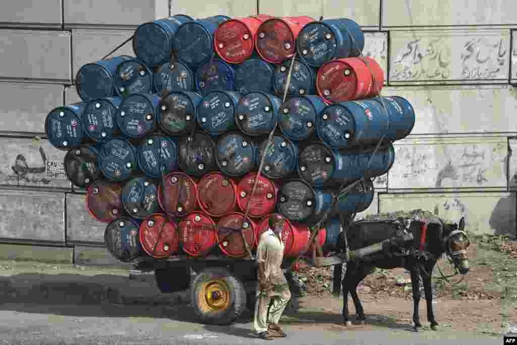 A man stands next to a horsecart laden with oil drums on a street in Lahore, Pakistan.