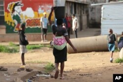In this Monday, April 6, 2020 photo, a woman carries a her baby and a bucket of water in Harare. Lockdowns imposed to curb the coronavirus’ spread have put millions of women in Africa, Asia and elsewhere out of reach of birth control. (AP Photo/Tsvangiray