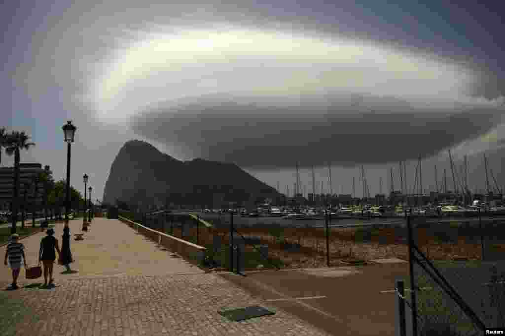 People walk along a street in front of the Rock of the British territory of Gibraltar (rear), a monolithic limestone promontory, next to the border in La Linea de la Concepcion, southern Spain.