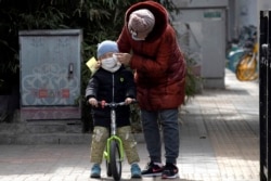 A woman wipes the face of a child on the streets of Beijing on Thursday, March 12, 2020. For most people, the new coronavirus causes only mild or moderate symptoms. (AP Photo/Ng Han Guan)