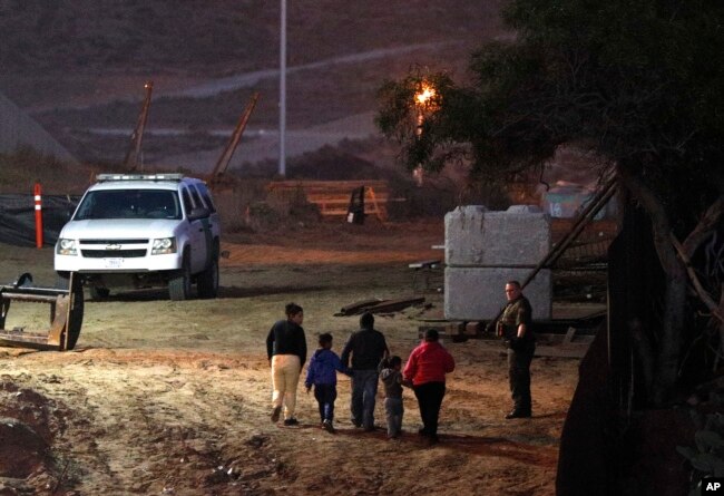 Migrants traveling with children walk up a hill to a waiting U.S. Border Patrol agent just inside San Ysidro, Calif., after climbing over the border wall from Playas de Tijuana, Mexico, Dec. 3, 2018.