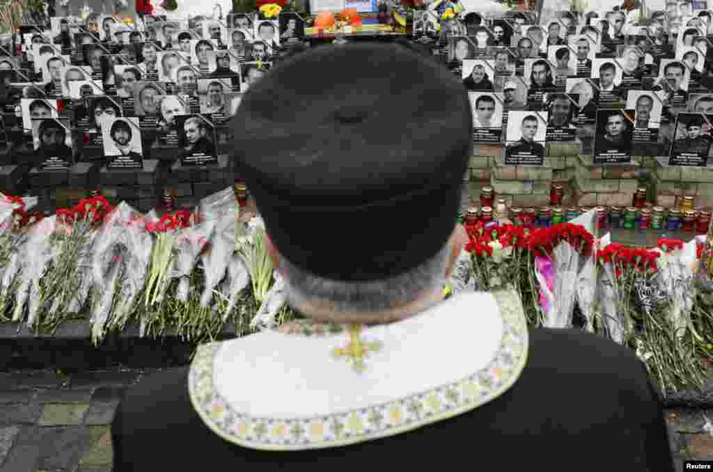 A clergyman stands near photos of people killed in anti-government protests in 2014, during a commemoration near Independence Square in Kyiv. Ukraine will mark the first anniversary of the ousting of the pro-Moscow President Viktor Yanukovich next weekend, honoring the memory of the 100 or so civilians killed in protests against him.