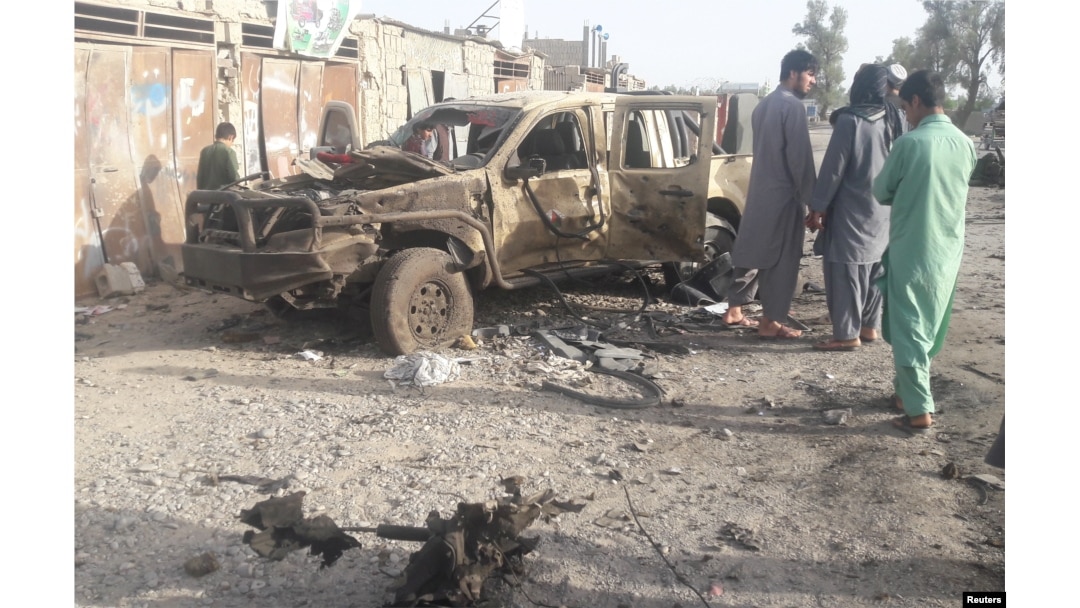 FILE - Residents look at an Army vehicle which was damaged during battle between Afghan security forces and Taliban in Farah province, Afghanistan, May 16, 2018.