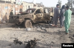 FILE - Residents look at an Army vehicle which was damaged during battle between Afghan security forces and Taliban in Farah province, Afghanistan, May 16, 2018.