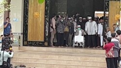 Abu Bakar Baasyir (tengah-duduk berkursi roda- baju putih) melambaikan tangan di hadapan para jurnalis dan masyarakat yang berada di pintu gerbang Ponpes Ngruki, Sukoharjo , Jumat (8/1). (Foto: VOA/ Yudha Satriawan)