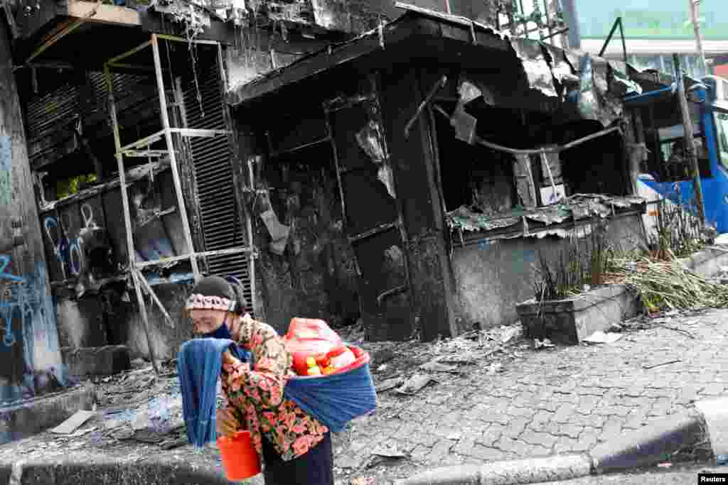 A traditional drink vendor reacts as she passes a burned police station a day after a protest against the government&#39;s jobs creation law which led to clashes between demonstrators and riot police near the Presidential Palace in Jakarta, Indonesia.