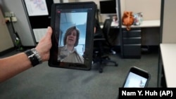 In this Friday, Aug. 13, 2021, photo Sheriff's Police Sgt. Bonnie Busching tests a video meeting from her personal electronic device with another person in the agency at the Cook County Sheriff's Office in Chicago. (AP Photo/Nam Y. Huh)