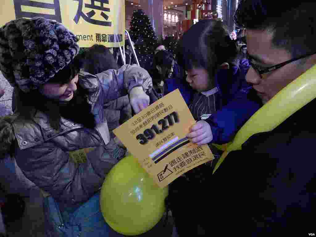 香港市民邱先生带同两岁的女儿参与工党除夕倒数活动，女儿手持呼吁年轻人登记做选民的传单