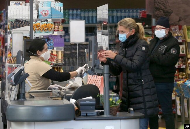 Supermarket employees and customers wear protective masks in a shop in Vienna, Austria, Wednesday, April 1, 2020.