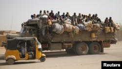Migrants sit on their belongings in the back of a truck as it is driven through a dusty road in the desert town of Agadez, Niger, headed for Libya, May 25, 2015. 