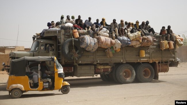 Migrants sit on their belongings in the back of a truck as it is driven through a dusty road in the desert town of Agadez, Niger, headed for Libya, May 25, 2015. 