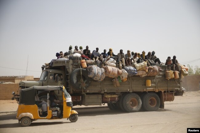 FILE - Migrants sit on their belongings in the back of a truck as it is driven through a dusty road in the desert town of Agadez, Niger, headed for Libya, May 25, 2015.
