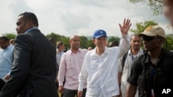 Sekretè Jeneral Nason, Zini Ban Ki-Moon, (sant) ak yon Kaskèt ble nan tèt li, kap salye popilasyon an pandan lansman an yon kanpay sanitasyon nan Henche, Ayiti, 14 Jiyè, 2014.