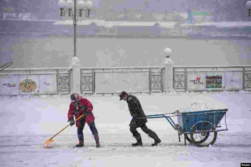 A cleaner pulls a cart as another shovels ice during heavy snow on a street in Jilin, Jilin province, China.