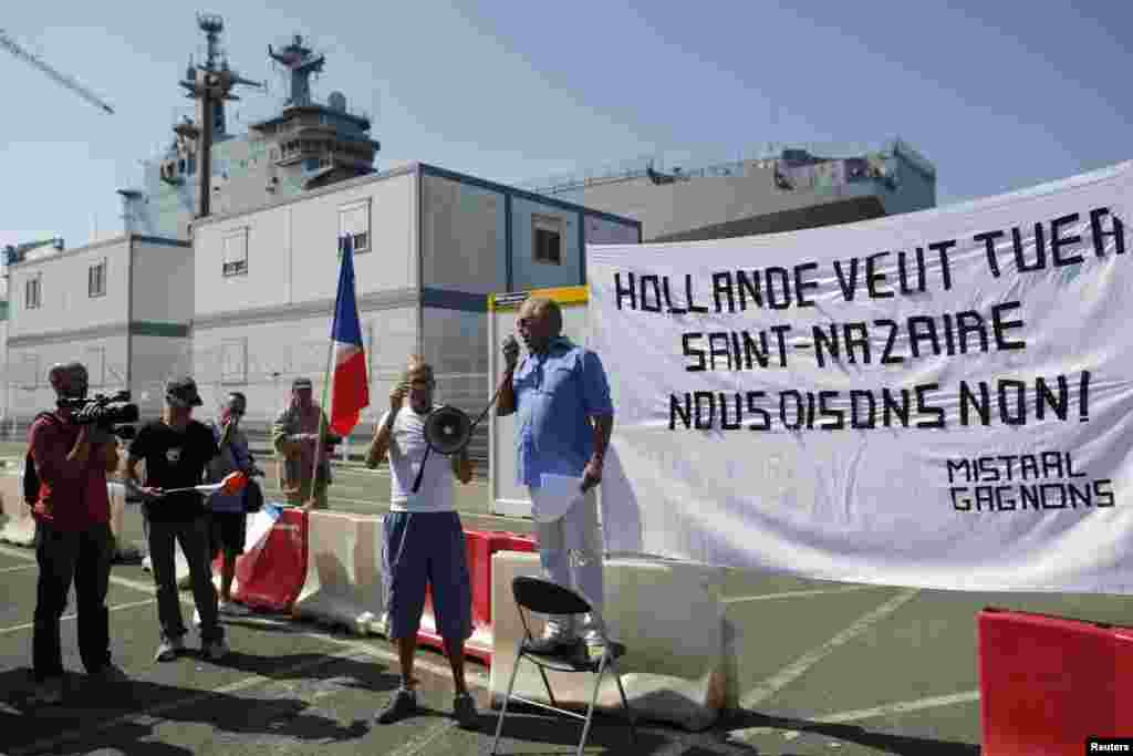 A man delivers a speech during a demonstration supporting a contract to deliver the Mistral-class helicopter carrier Vladivostok warship to Russia (seen in the background), at the STX Les Chantiers de l'Atlantique shipyard site in Saint-Nazaire, Sept. 7, 