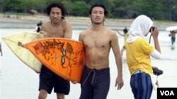 Dua turis Jepang berjalan di pinggiran pantai Kuta, Bali, usai berselancar. (Foto: Dok)