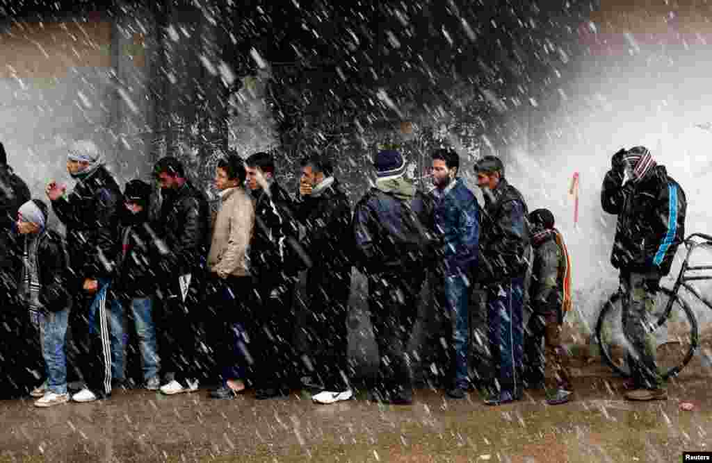 Men wait to buy bread in front of a bakery shop in Al Qusayr, western Syria.