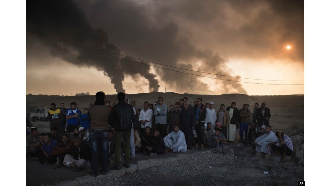 Men are held by Iraqi national security agents, to be interrogated at a checkpoint, as oil fields burn in Qayyarah, south of Mosul, Iraq, Nov. 5, 2016.