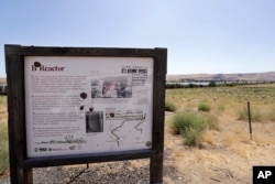 In this photo taken Aug. 14, 2019, a roadside sign on the Hanford Reach National Monument gives information about the Hanford Nuclear Reservation in view on the other side of the Columbia River flowing past near Richland, Wash. (AP Photo/Elaine Thompson)