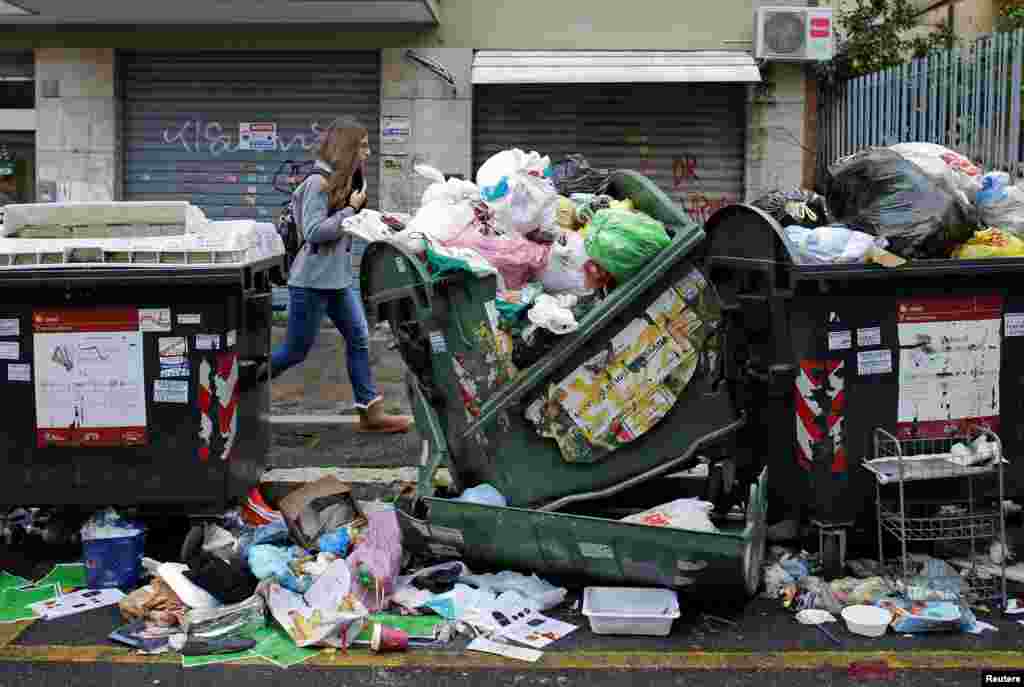 A woman walks next to garbage bins in Rome, Italy.